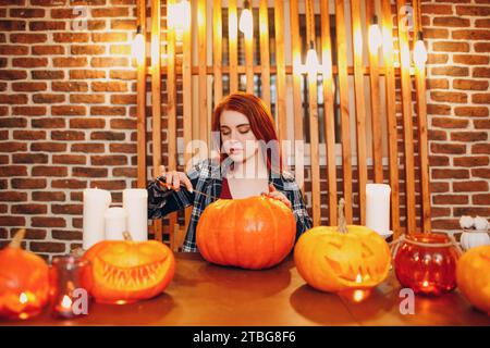 Jeune femme faisant la citrouille d'Halloween Jack-o-lanterne.Les mains de femmes coupantes des citrouilles avec un couteau Banque D'Images