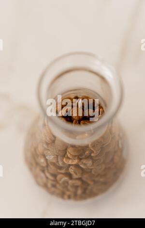 Un petit bocal en verre rempli de grains de café torréfiés sur une table blanche Banque D'Images