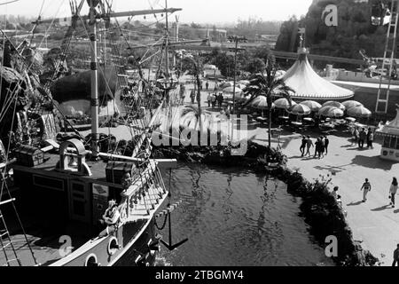 Blick über den Bug des Piratenschiffes Chicken of the Sea im Bereich Fantasyland von Disneyland Anaheim, im hintergrund ein Pavillon mit Tischen und Schirmen sowie ein Teil des Matterhorn und der Fahrbahn des Monorail, 1962. Vue à travers la proue du bateau pirate Chicken of the Sea dans la zone Fantasyland de Disneyland Anaheim, avec un pavillon avec des tables et des parasols et une partie de la piste du Cervin et du monorail en arrière-plan, 1962. Banque D'Images