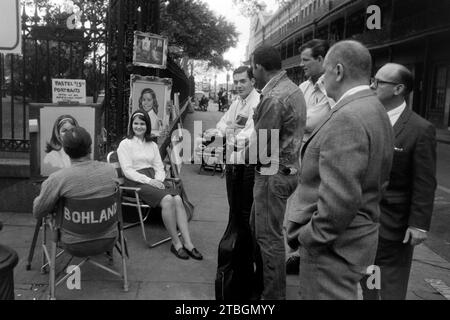 Junge Männer sehen einem Porträtzeichner im French Quarter dabei zu, wie er das Bildnis einer jungen Frau mit Pastellkreiden anfertigt, Nouvelle-Orléans 1965. De jeunes hommes regardent un portraitiste dans le quartier français faire un portrait d'une jeune femme au pastel, Nouvelle-Orléans 1965. Banque D'Images