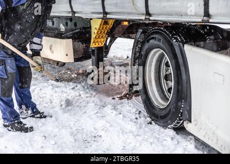 Le travailleur aide le camion à sortir de la neige, en utilisant une pelle et du sable. Banque D'Images