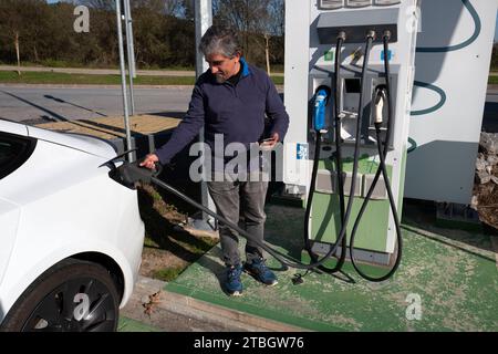 Homme branché une prise CCS à sa voiture électrique Tesla Model 3 à une borne de recharge rapide publique Banque D'Images