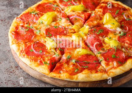Pepperoncini Pizza avec salami, herbes et oignons rouges gros plan sur une planche de bois sur la table. Horizontal Banque D'Images