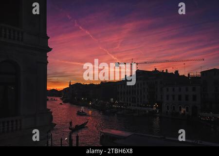 Un coucher de soleil rouge spectaculaire sur le Grand Canal au sud-ouest du Rialto, un reflet rouge sur l'eau, une gondole en silhouette ramait sur l'eau taquetée Banque D'Images