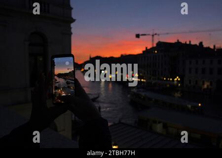 Une caméra de téléphone capture un coucher de soleil rouge sur le Grand Canal à Rialto regardant au sud-ouest, reflet rouge sur l'eau, une gondole en silhouette le canal Banque D'Images