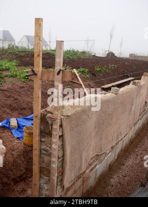 Mur d'enceinte avec façade traditionnelle en pierre en cours de construction dans un nouveau développement immobilier. Hessian protège la nouvelle maçonnerie du froid. Banque D'Images