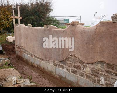Mur d'enceinte avec façade traditionnelle en pierre en cours de construction dans un nouveau développement immobilier. Hessian protège la nouvelle maçonnerie du froid. Banque D'Images