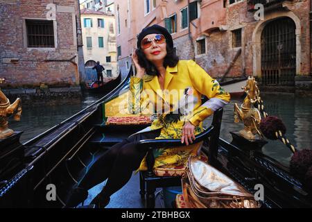 Une femme élégante portant un manteau oriental dans une gondole avec des chevaux dorés ramés devant l'architecture vénitienne sur les canaux pittoresques de Venise, en Italie Banque D'Images