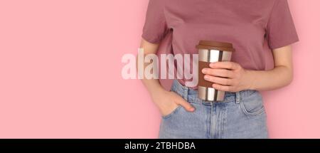 Bannière avec femme tenir dans les mains tasse à café réutilisable devant le fond rose. Concept de boissons à emporter avec espace de copie. Mise au point sélective. Banque D'Images