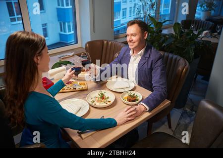 Femme et homme tenant la main et clinquant des verres à table pendant le dîner du nouvel an Banque D'Images