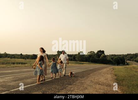 Maman, papa et filles marchent l'un après l'autre le long d'une route rurale le long de la forêt. Une famille heureuse Banque D'Images