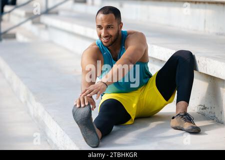 Jeune homme en vêtements de sport s'exerçant et faisant des étirements de jambes Banque D'Images