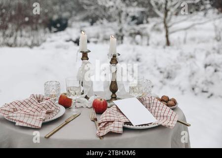 Dîner romantique pour deux. Agencement de table de Noël en plein air. Verre de vin, bougies et serviettes à carreaux. Mariage d'hiver, Saint Valentin ou anniversaire Banque D'Images