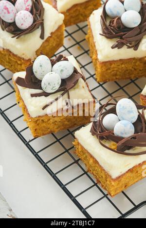 Barres de gâteau aux carottes de Pâques décorées avec nid de chocolat et œufs de bonbons au chocolat fleurissant des fleurs de cerise ou de pomme sur des fonds rustiques en bois clair. Banque D'Images