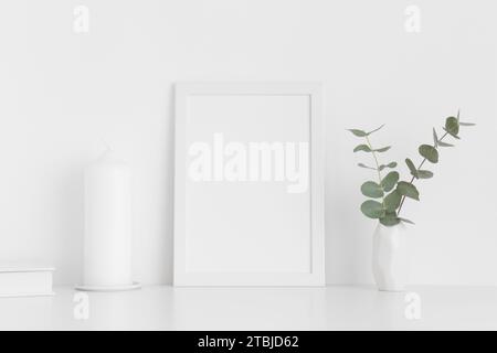 Maquette de cadre blanc avec accessoires d'espace de travail et eucalyptus dans un vase sur une table blanche. Orientation portrait. Banque D'Images