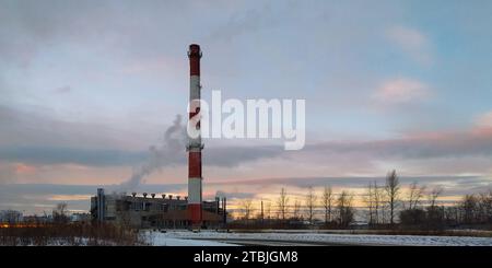 Chaufferie avec une grande cheminée à fumer rayée au milieu d'un paysage de soirée d'hiver Banque D'Images