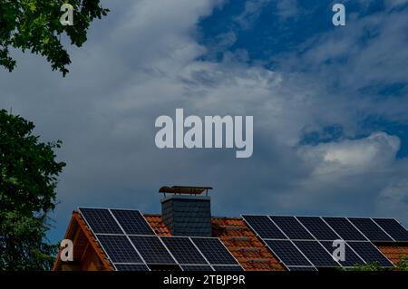 Toit d'une maison unifamiliale pleine de panneaux solaires avec un ciel bleu nuageux et quelques feuilles vertes en arrière-plan Banque D'Images
