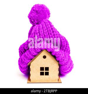 Maison en bois jouet portant un chapeau tricoté violet prêt pour l'hiver. Charme saisonnier et concept lié aux vibrations de vacances. Banque D'Images