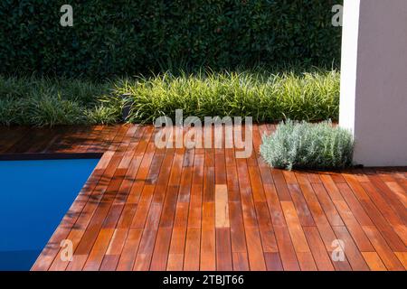 Plancher de bois de terrasse de piscine avec gommage de clôture à feuilles persistantes, herbe et pilier blanc, idée d'intimité de la piscine Banque D'Images