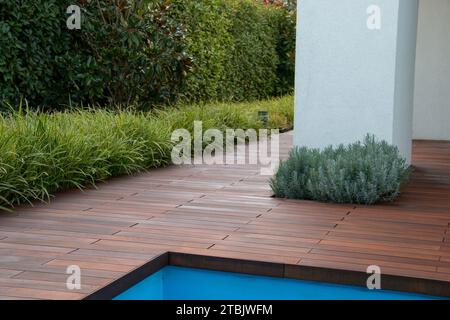 Plancher de bois de terrasse de piscine avec gommage de clôture à feuilles persistantes, herbe et pilier blanc, idée d'intimité de la piscine Banque D'Images