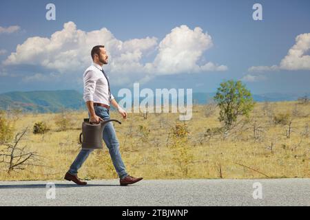 Homme d'affaires marchant avec une cartouche d'essence sur une route Banque D'Images