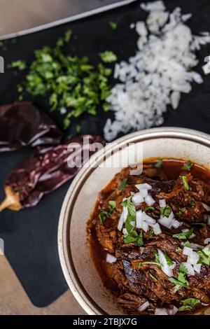 Un bol de viande de bœuf bigria cuite lentement et braisée dans un bol d'époque avec des oignons hachés, de la coriandre, des poivrons guajillo et du bouillon Banque D'Images