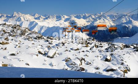 Orange chairlift with unrecognizable skiers in Samnaun - Ischgl - Paznaun ski resort, located in Austria and Switzerland. Winter, ski, chair lift. Banque D'Images