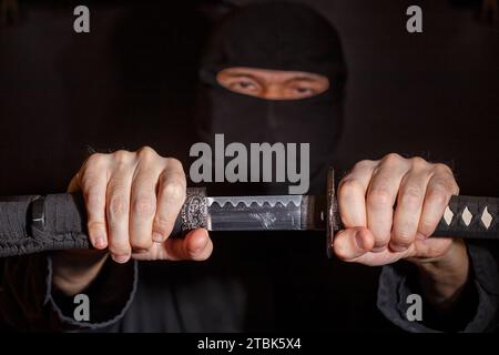 Ninja prêt à combattre, tenant une épée japonaise.Photo d'un guerrier vêtu de vêtements noirs et d'un visage fermé Banque D'Images