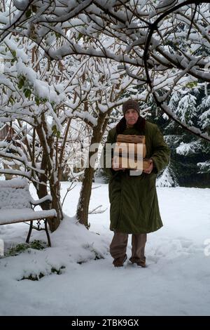 Homme transporter le bois à travers la neige qui tombe dans le jardin d'utiliser comme combustible dans un poêle à bois zala hongrie Banque D'Images