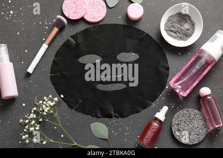 Masque de drap facial avec différents produits cosmétiques et fleurs de gypsophila sur fond noir Banque D'Images