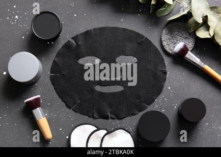 Masque de drap facial avec différents produits cosmétiques et eucalyptus sur fond noir Banque D'Images