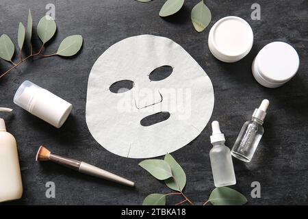 Masque de drap facial avec différents produits cosmétiques et eucalyptus sur fond noir Banque D'Images