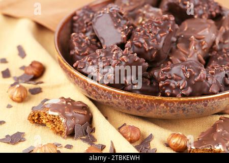 Biscuits au chocolat avec noisettes dans un bol en céramique sur le fond de tissu brun. Banque D'Images