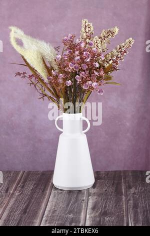 Fleurs artificielles dans un vase blanc sur fond de tissu rose. Banque D'Images