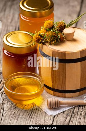 Miel dans des bols transparents, pots, tonneau en bois et fleurs sur un fond en bois rustique. Concept de produits apicoles biologiques naturels. Banque D'Images