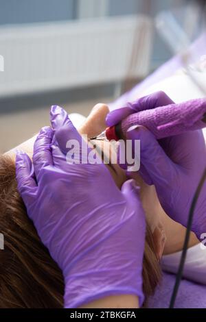 Maître de beauté effectue le maquillage permanent des sourcils dans un salon de beauté, close-up. Mains d'un cosmétologue faisant du microblading des sourcils. Tatouage sur le fa Banque D'Images