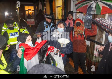 Mirfield, Royaume-Uni. 07 DÉCEMBRE 2023. Un groupe de manifestants se tient sur les marches du Old Bank Working Man Club (89 Old Bank Rd, Mirfield WF14 0HY) pour protester contre l'événement de collecte de fonds du parti travailliste qui se déroule là-bas, avec Kim Leadbeater, députée travailliste de Batley et Spen et Angela Rayner, vice-premier ministre fantôme du Royaume-Uni. Environ 15 militants ont chanté pendant 2 heures avec une présence policière importante, tandis que 2 manifestants sont entrés brièvement dans les locaux sans arrestation. Crédit Milo Chandler/Alamy Live News Banque D'Images