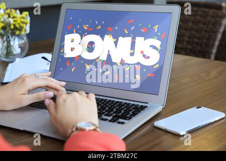 Gain de bonus. Femme utilisant un ordinateur portable à la table en bois à l'intérieur, closeup. Illustration de la chute de confettis et mot sur l'écran de l'appareil Banque D'Images