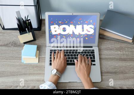 Gain de bonus. Femme utilisant un ordinateur portable à la table en bois, vue au-dessus. Illustration de la chute de confettis et mot sur l'écran de l'appareil Banque D'Images