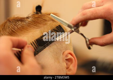 Coiffeur professionnel coupant les cheveux de garçon dans le salon de beauté, closeup Banque D'Images