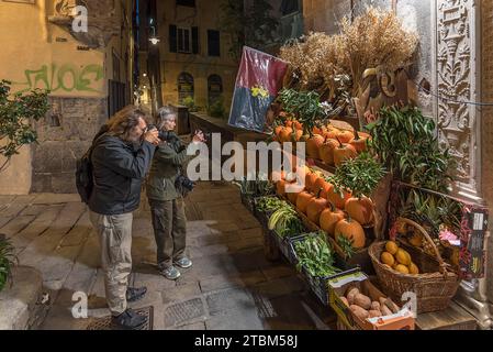 Touristes photographiant un magasin de fruits dans la soirée dans le centre historique, Gênes, Italie Banque D'Images