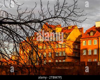 Les bâtiments historiques, les murs en brique rouge de barbacane de Varsovie, Pologne et la silhouette d'une branche d'arbre en face d'eux au coucher du soleil au printemps Banque D'Images