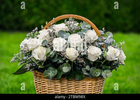 Bouquet de belles roses blanches dans un panier en osier sur fond vert. Idéal pour les cartes de vœux Banque D'Images