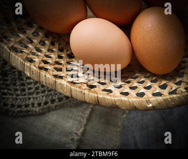 Vue de dessus d'oeufs dans un panier de paille sur une des serviettes en lin naturel et un fond de bois rustique Banque D'Images