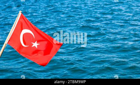 Drapeau national de la Turquie sur un mât dans le vent sur un fond de mer bleue Banque D'Images