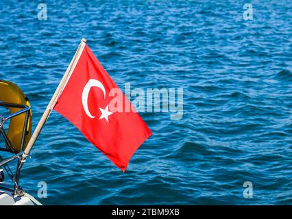 Drapeau national de la Turquie sur un mât dans le vent sur un fond de mer bleue Banque D'Images