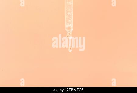 Pipette cosmétique avec une goutte transparente de sérum gros plan sur fond rose Banque D'Images