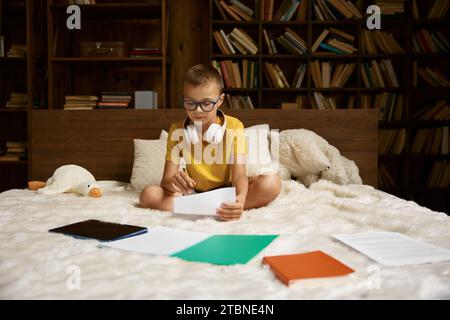 Petit garçon enfant étudiant à la maison couché dans le lit Banque D'Images