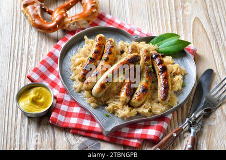 Six saucisses de Nuremberg frites à la choucroute sur une assiette en étain en forme de cœur, servies avec de la moutarde et un bretzel bavarois Banque D'Images