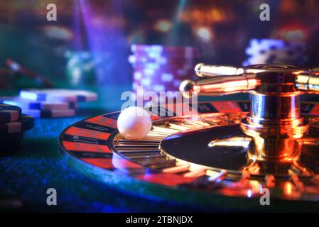 Détail d'une boule fixe sur un numéro de roulette de casino sur un tapis de jeu avec des jetons de pari autour d'elle et lumières dans une salle de jeu sombre Banque D'Images